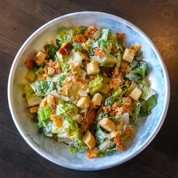 A Caesar salad with romaine lettuce, croutons, and parmesan cheese in a light blue bowl.