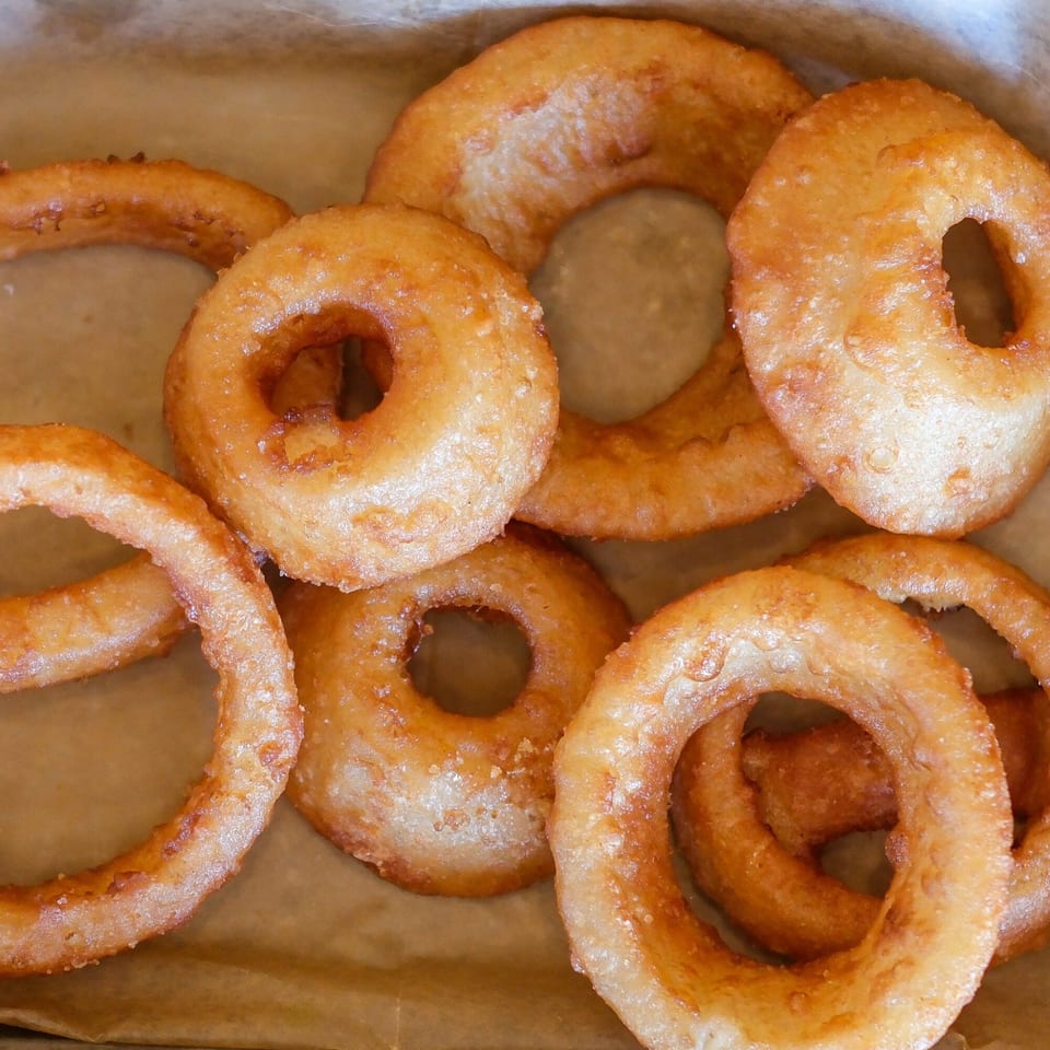 Close-up of golden-brown, crispy onion rings from The Outsider, served in a paper-lined basket.