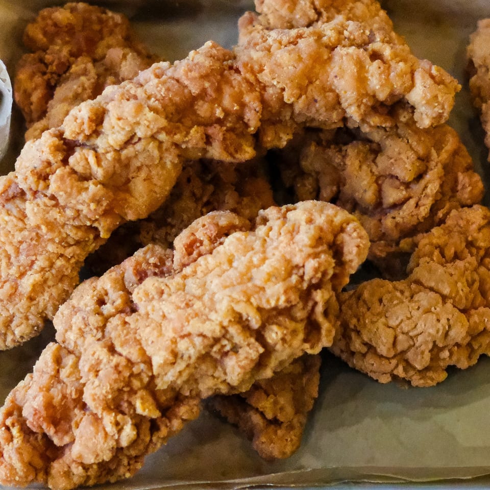 Close-up of golden-brown, crispy fried chicken tenders from The Outsider, a burger restaurant.