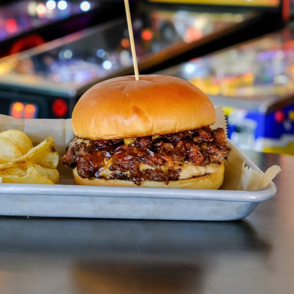 A juicy Outsider burger with melted cheese and BBQ sauce, served with potato chips on a metal tray.