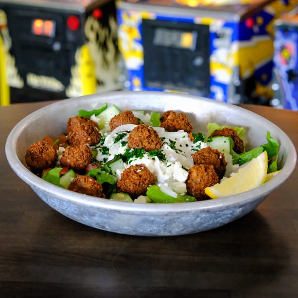 Falafel salad with feta, greens, and lemon in a metal bowl on a dark wooden table.