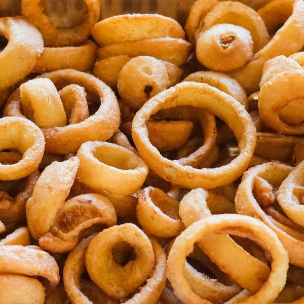 Close-up of golden-brown, crispy onion rings, some lightly dusted with seasoning, from The Outsider.