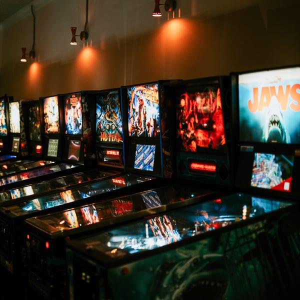 Row of illuminated pinball machines with various movie themes, including Jaws, in a dimly lit arcade.