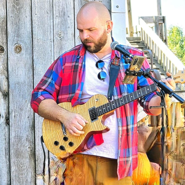 A musician playing an electric guitar and singing into a microphone at The Outsider.