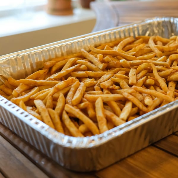 A large aluminum tray filled with golden-brown, seasoned french fries from The Outsider.