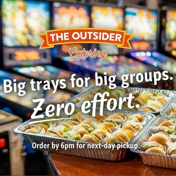 The Outsider catering trays filled with mini burgers, with pinball machines in the background.